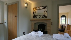 A hotel room with a large bed, a fireplace, a wooden door, and a mirror on the wall.