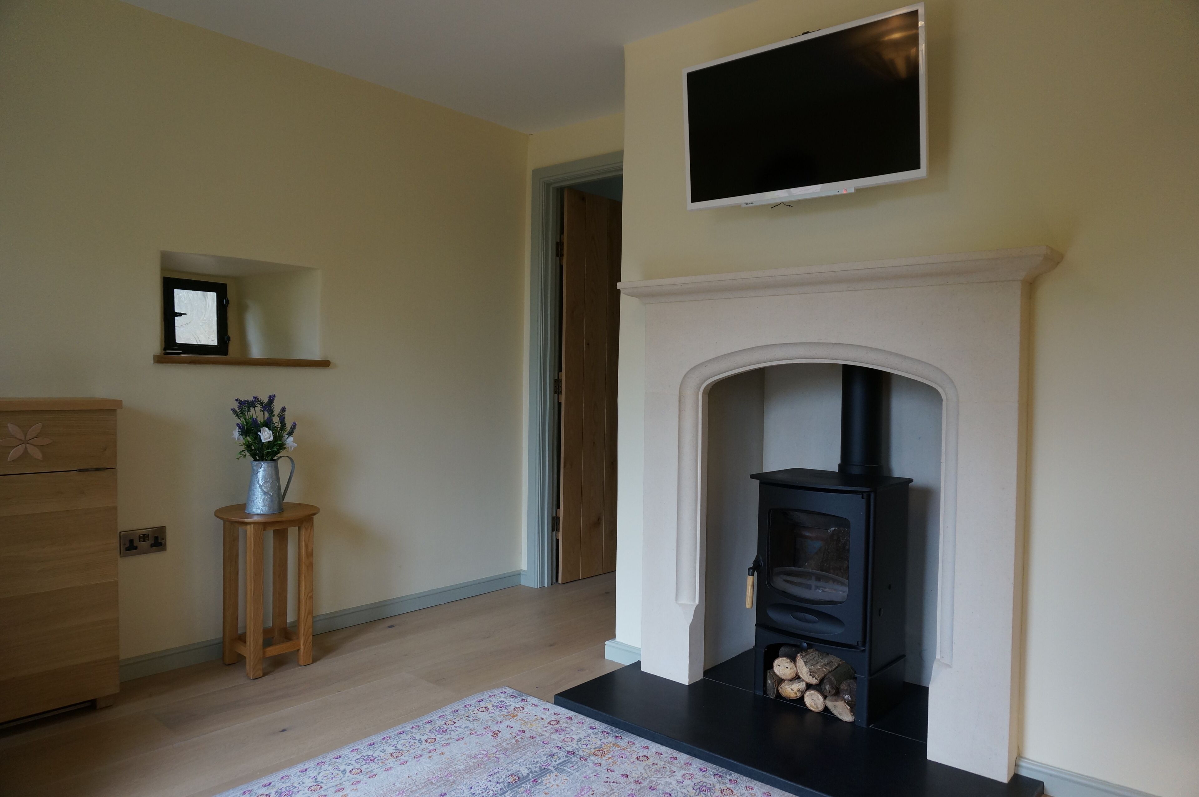 A living room with a fireplace, a television mounted above it, a wooden dresser, and a small table with a vase.