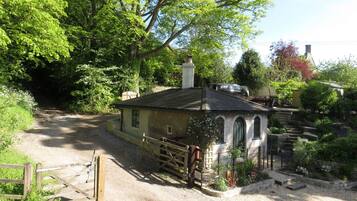 A rustic house with a stone pathway leading to a gated entrance, surrounded by lush greenery and a small garden.