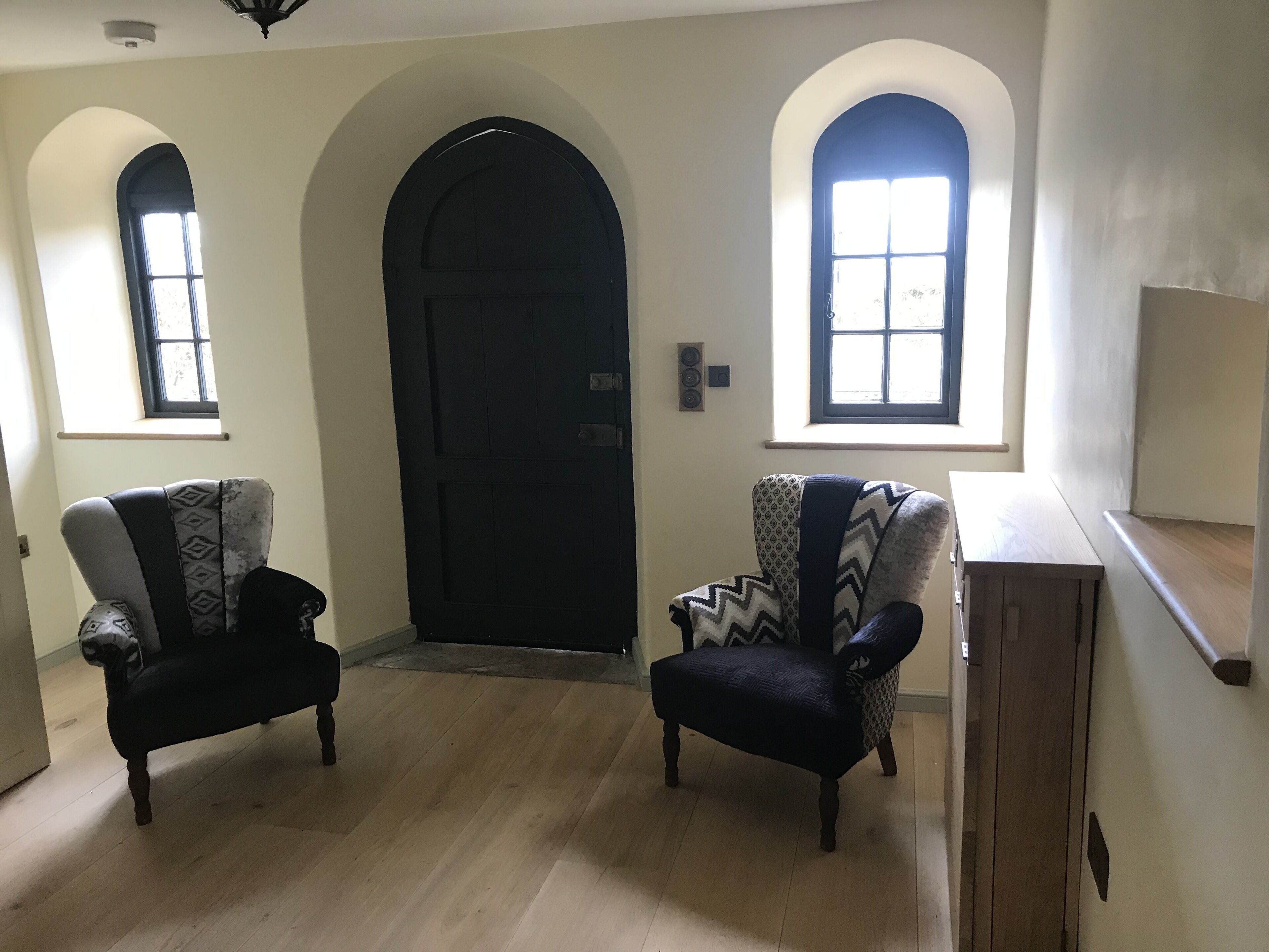 A room with a black door, two armchairs with patterned upholstery, and a wooden bench.