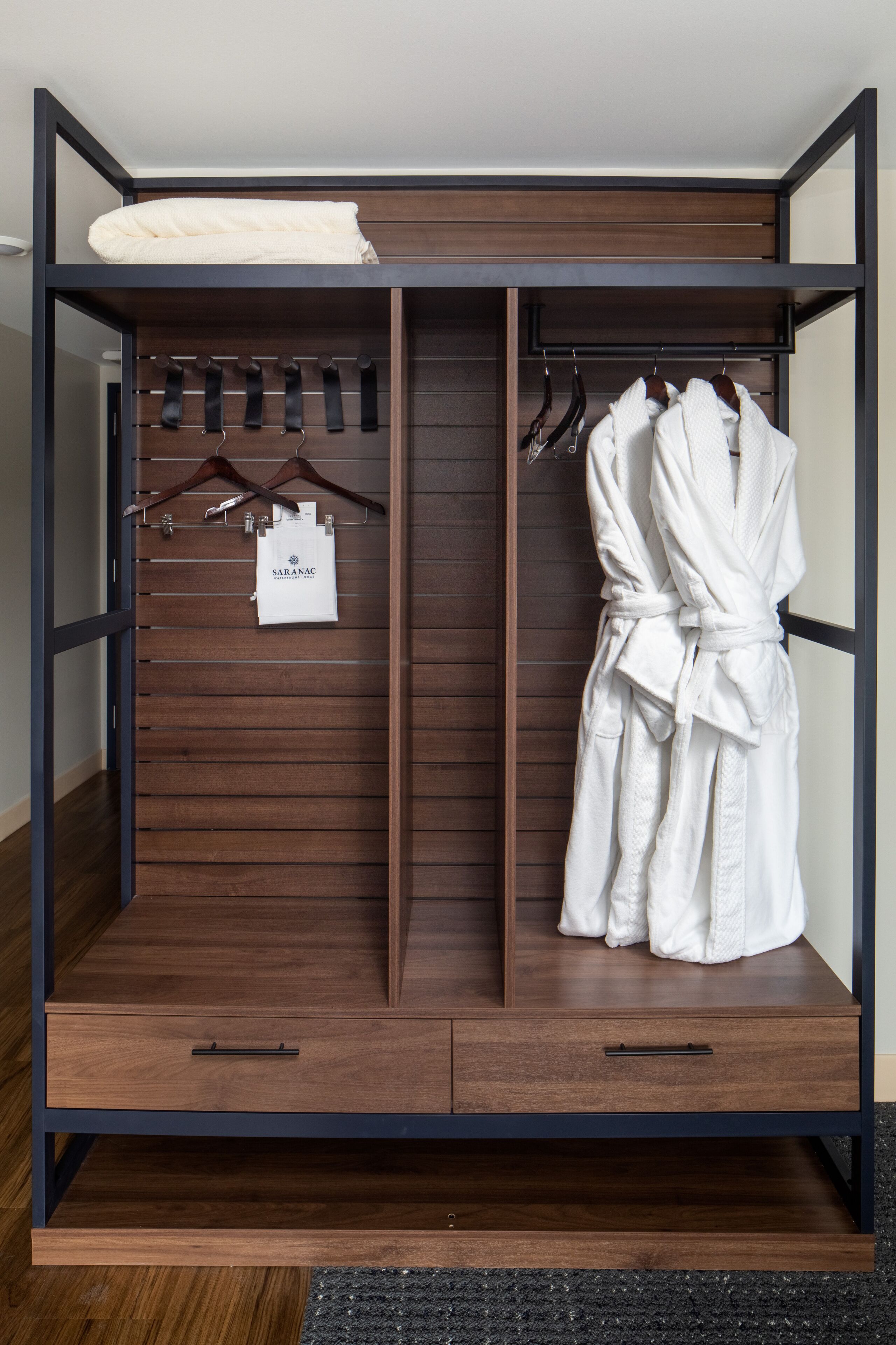 A walk-in closet with wooden shelves, a robe hanging, and a folded towel on the top shelf.