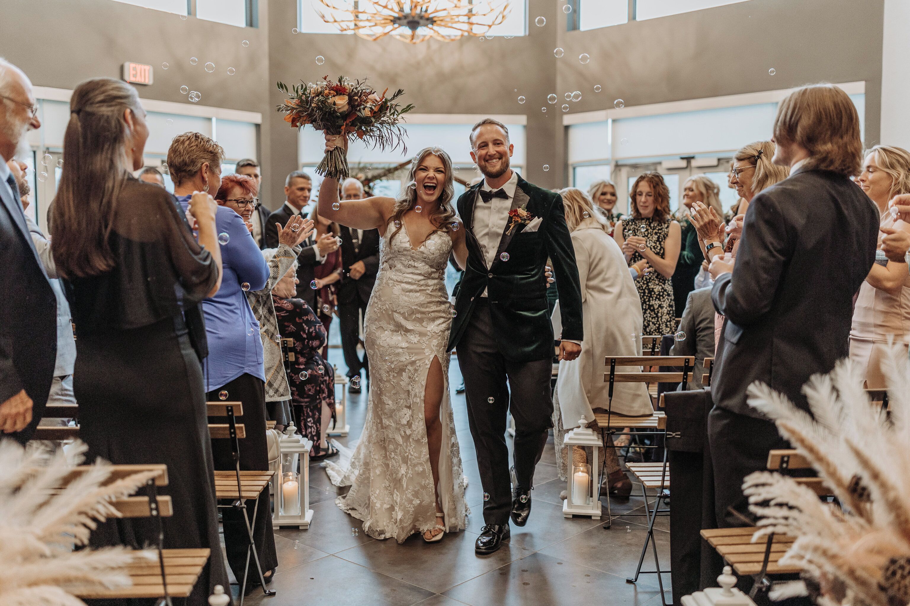 Una ceremonia de boda con invitados sentados en bancas de madera, un candelabro sobre ellos y una decoración floral al frente.