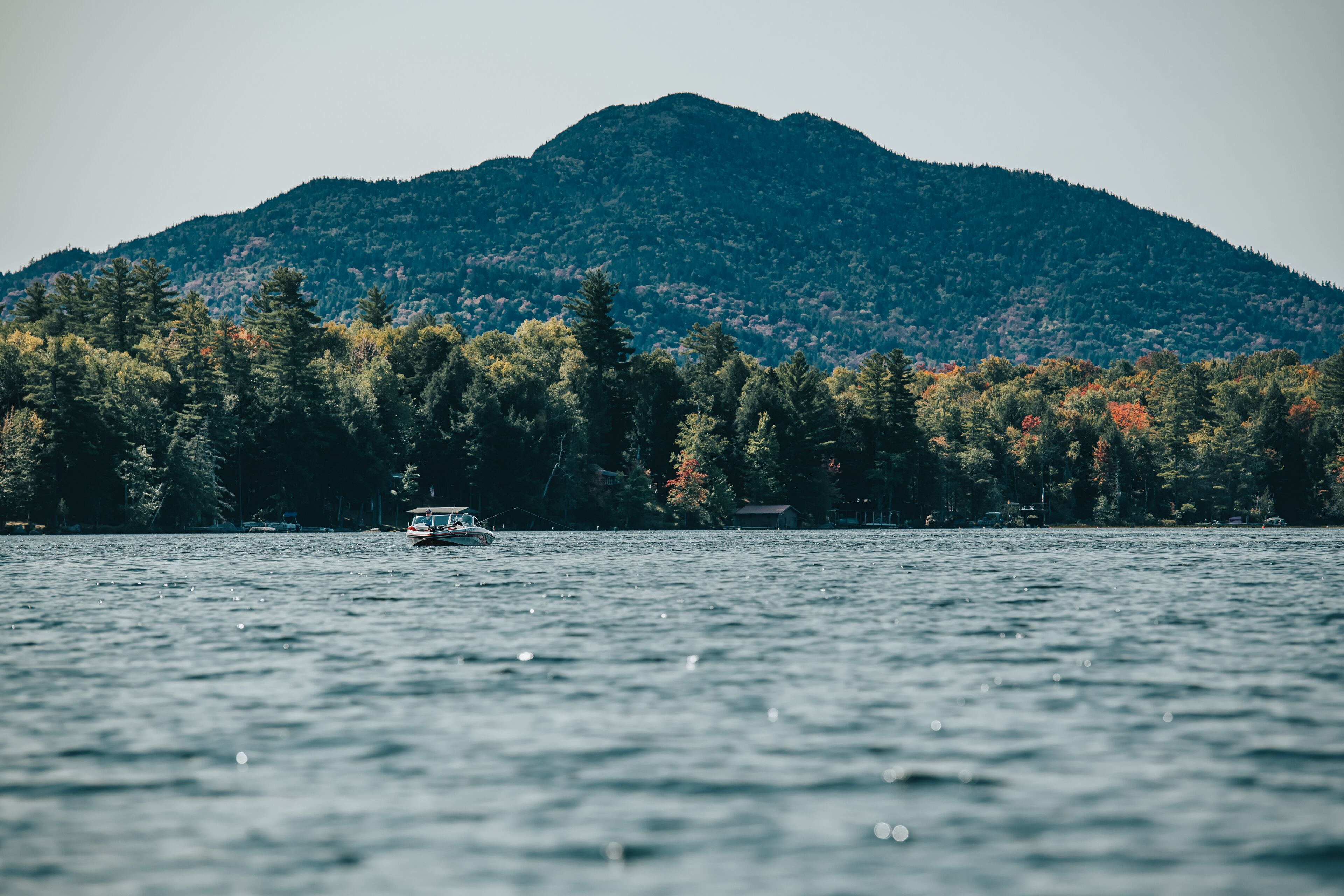 A boat on a calm lake with a forested mountain in the background.