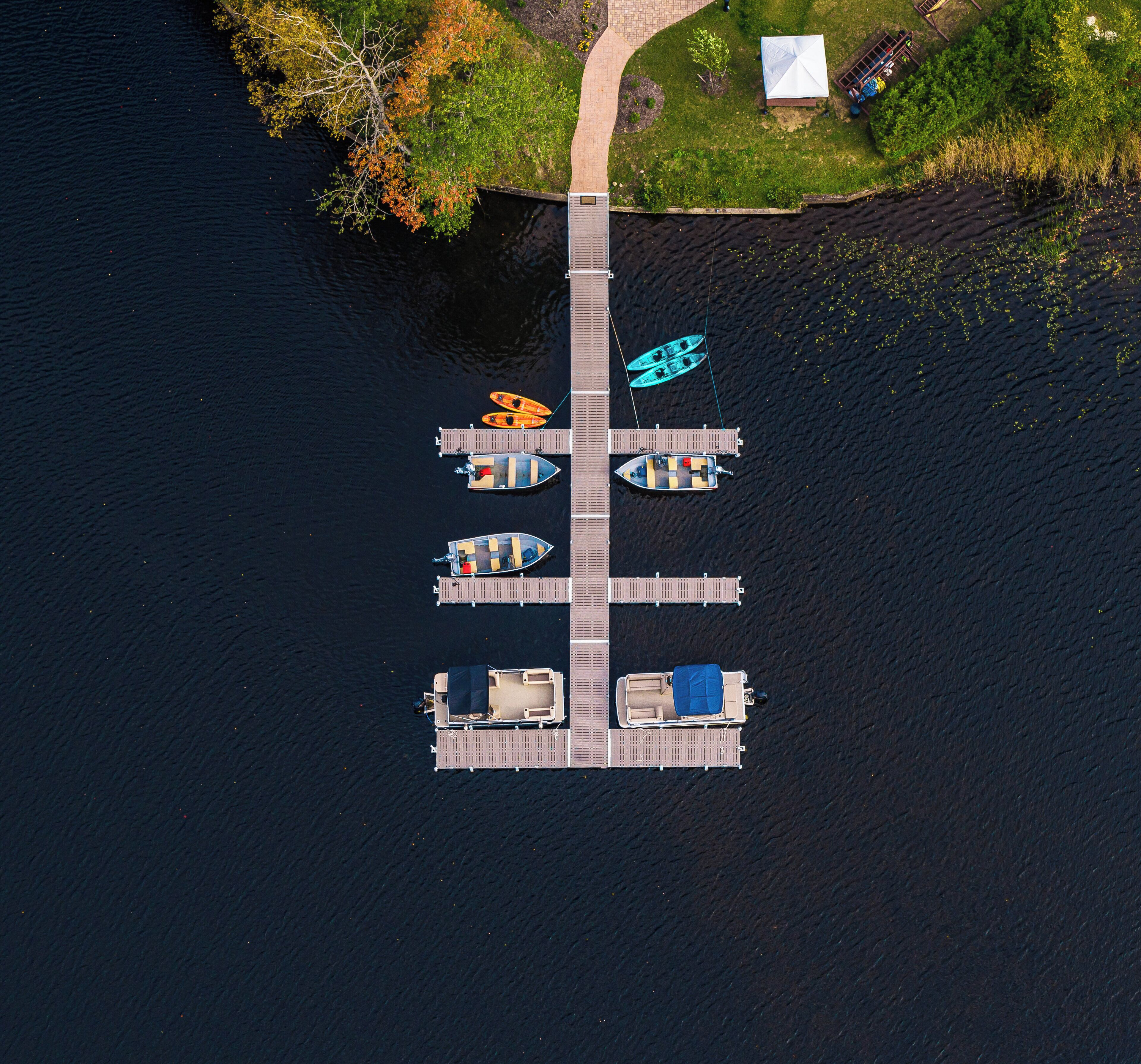 An aerial view of a dock with five boats, a grassy area with a building, and a body of water.