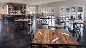A spacious restaurant with multiple wooden tables and chairs, a bar area, and large windows offering views of a lake.