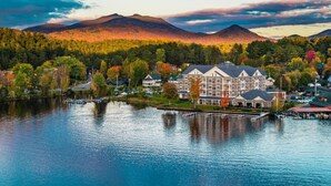 A large, multi-story hotel with a waterfront view, situated on a lakeside with mountains in the background. - voco Saranac Lake NY - Waterfront by IHG (Saranac Lake)