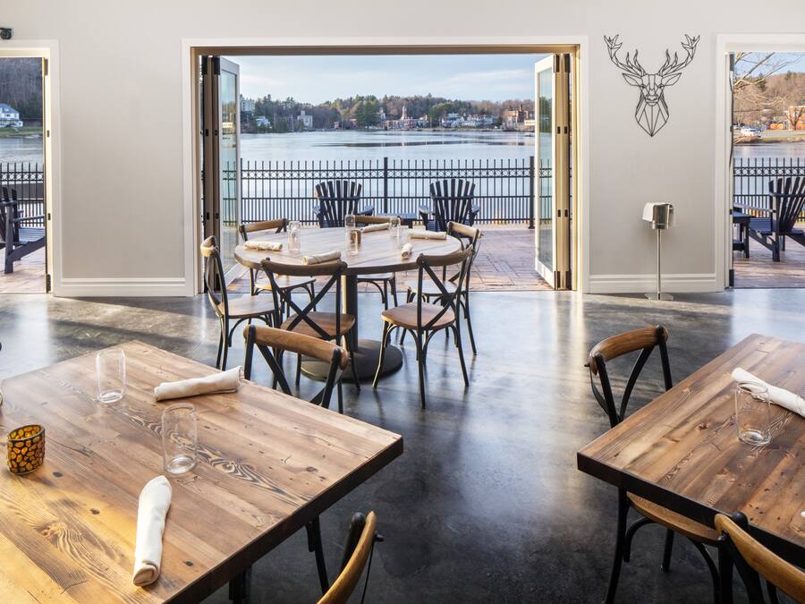 Un comedor con mesas y sillas de madera, vistas a un lago y una decoración de cabeza de ciervo en la pared.