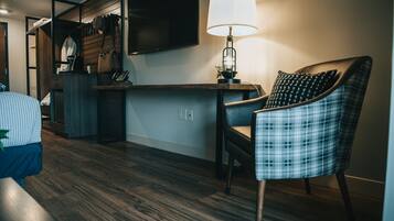 Un salón moderno con suelo de madera, un sillón escocés, un escritorio con lámpara y un televisor de pared.