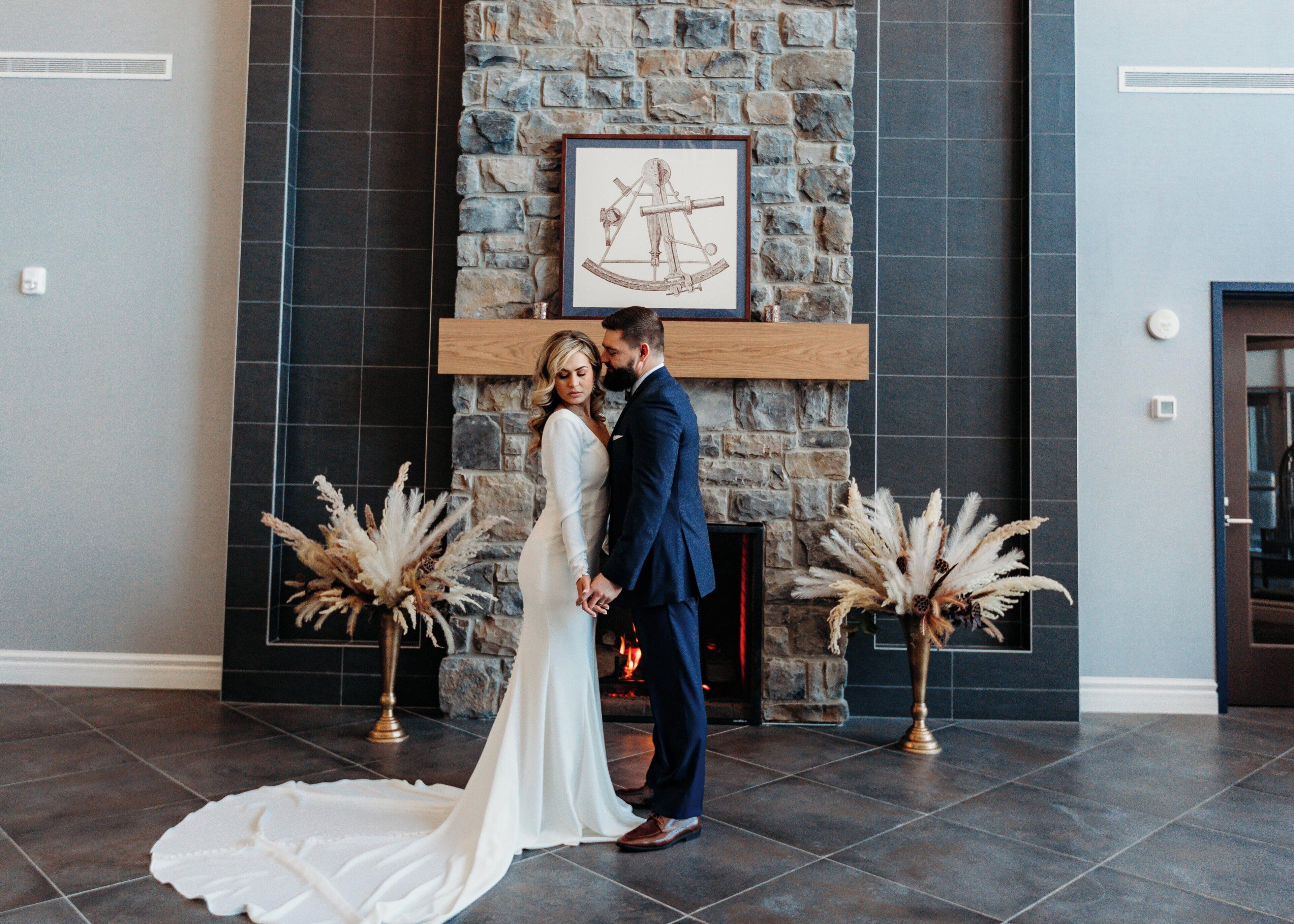 A couple standing in a room with a stone fireplace, holding hands.