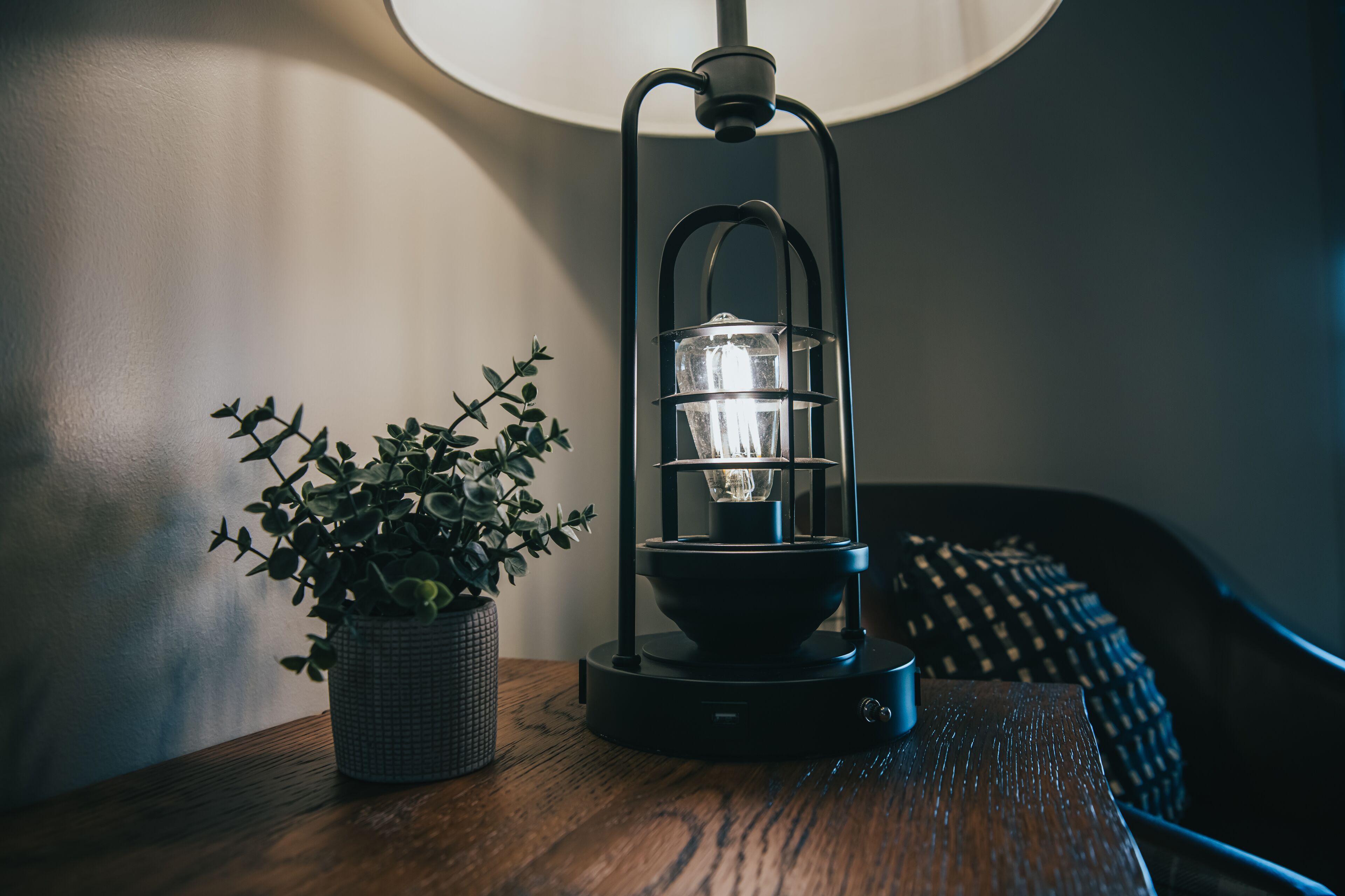 A table with a black lantern-style lamp and a potted plant.
