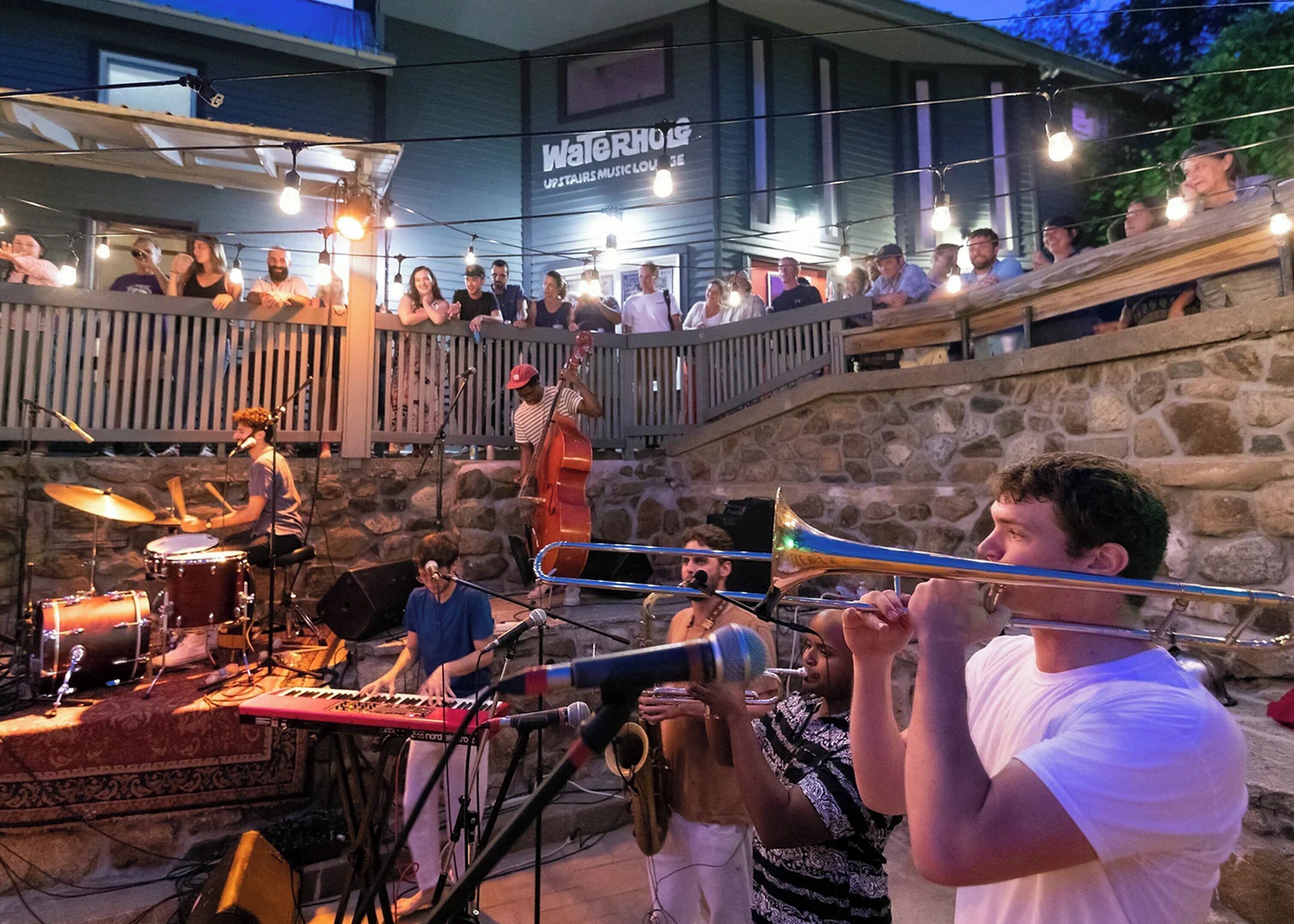 Evento musical al aire libre con un escenario, músicos y un público.