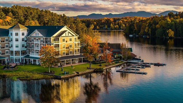 A lakeside hotel with multiple buildings, a dock, and a reflection in the water. - voco Saranac Lake NY - Waterfront by IHG (Saranac Lake)