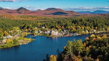 A lakeside town with houses and a large building, surrounded by mountains and autumn foliage.