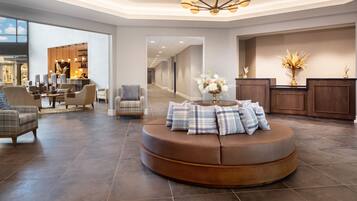 A spacious lobby with a round seating area, a reception desk, and a view into the dining area.