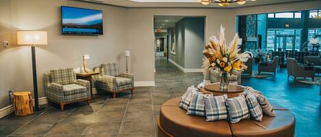 A lobby with a brown leather sofa, plaid chairs, a flat-screen TV, and a large window.