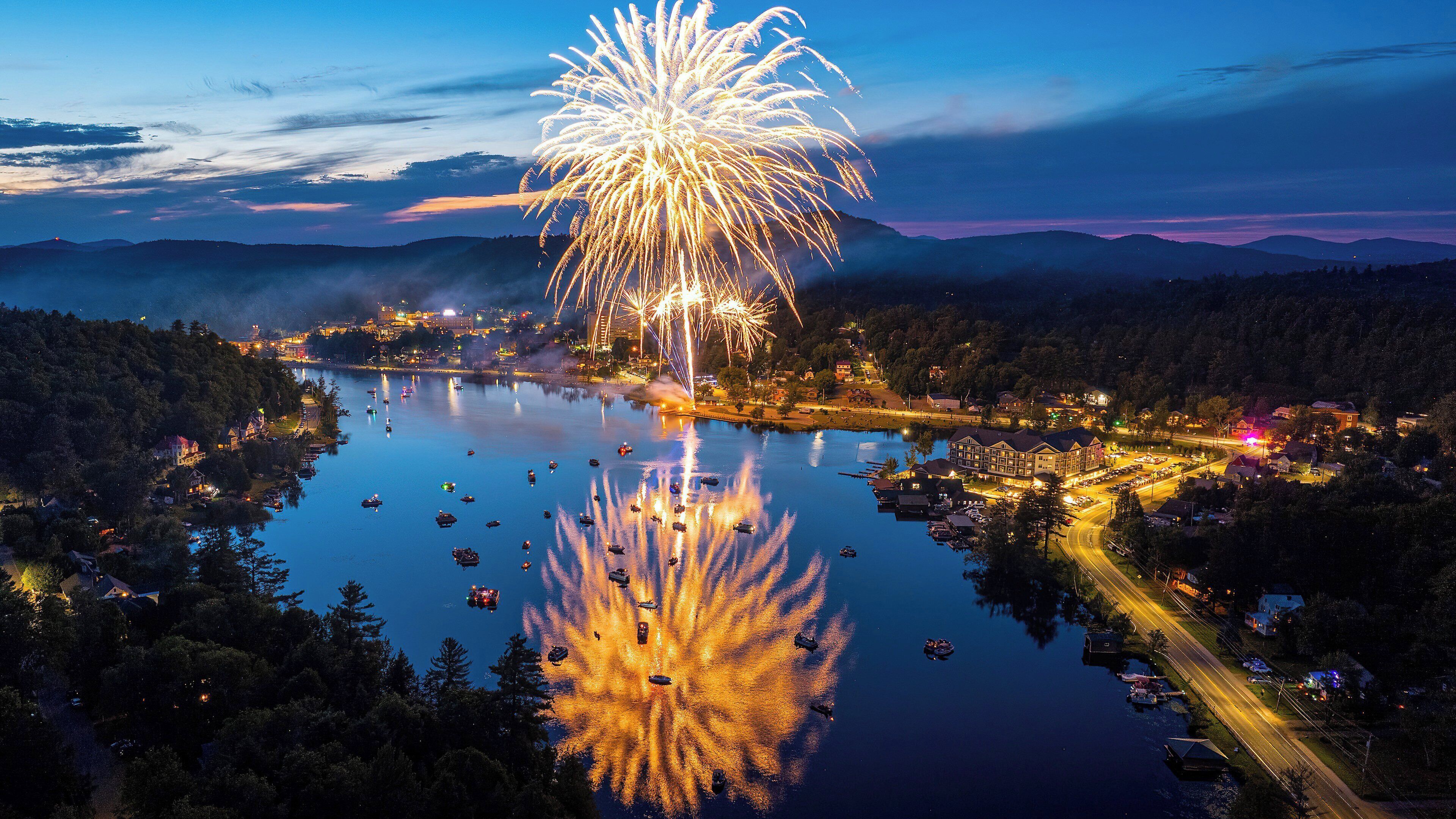 Un pueblo a orillas del lago con un edificio destacado reflejando fuegos artificiales.