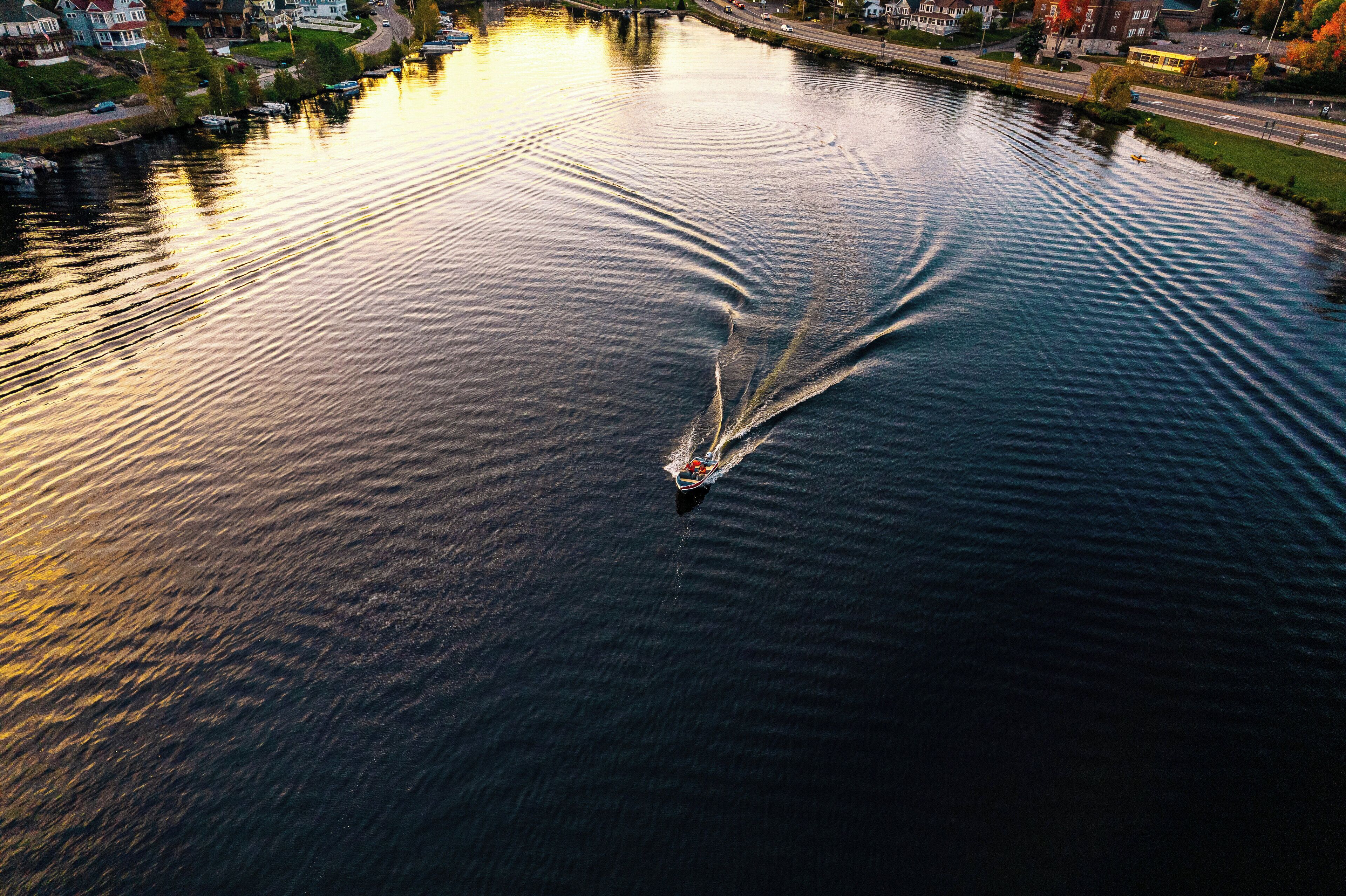 Un bote navegando por un río tranquilo, con reflejos de edificios y árboles en el agua.