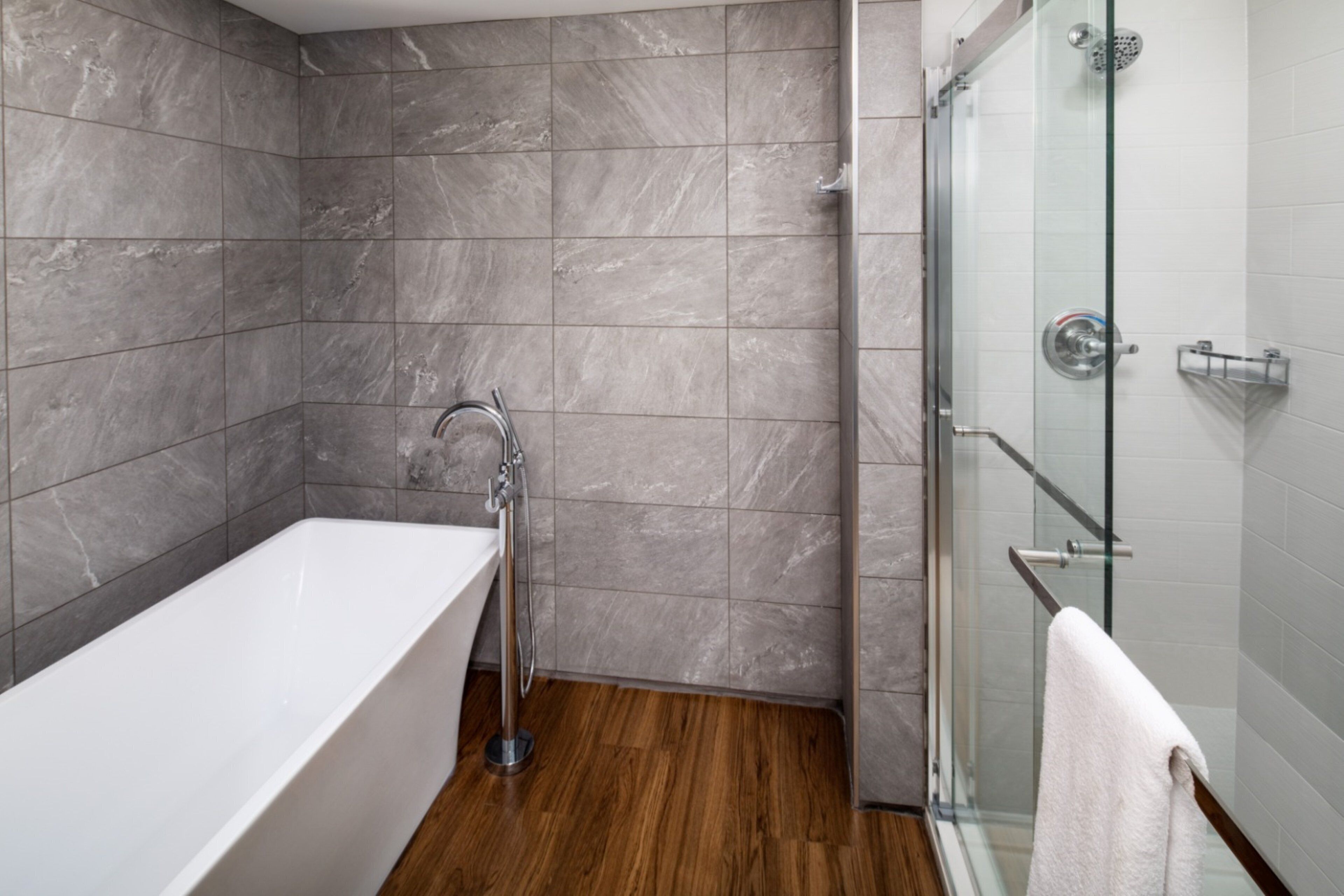 Une salle de bain moderne avec une baignoire sur pieds, une douche en verre et un plancher en bois.