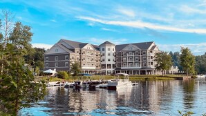 A large, multi-story hotel with a waterfront view, docked boats, and a serene lake setting. - voco Saranac Lake NY - Waterfront by IHG (Saranac Lake)