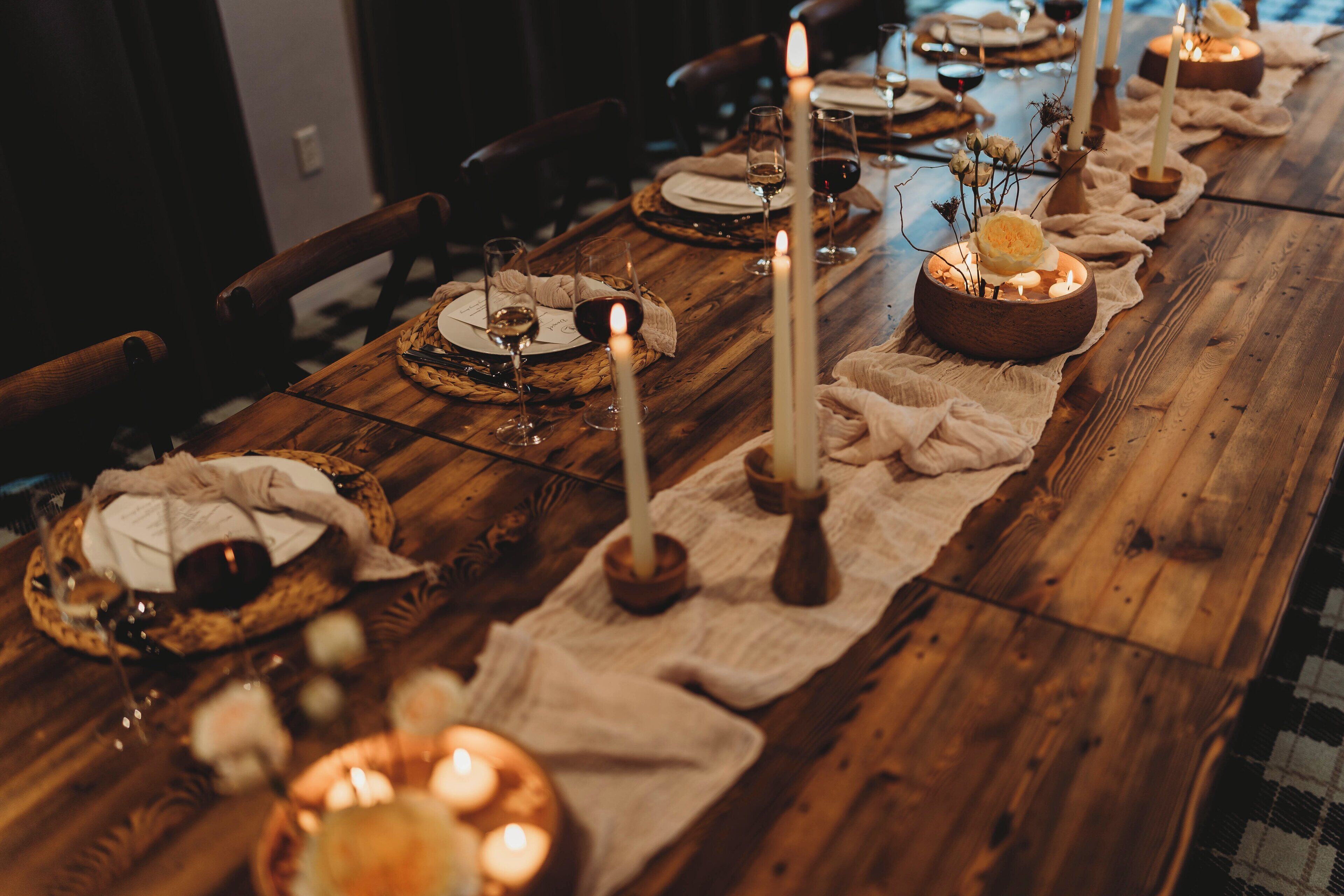 A long wooden table set for a meal with candles, plates, and glasses.