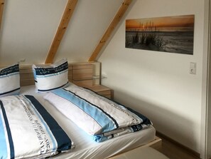 Cozy loft-style bedroom with a sloped ceiling, featuring a neatly made bed and a bedside table with a lamp.