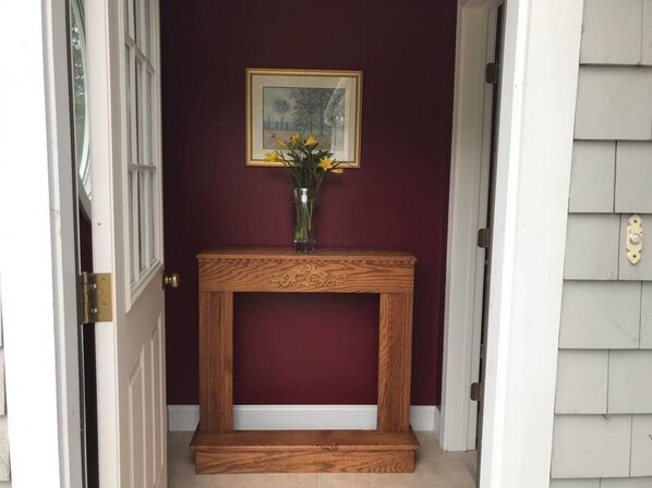 A wooden console table with a vase of yellow flowers against a maroon wall.
