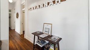 A hallway with a wooden floor, a white wall with the word "SAVANNAH" spelled out, and a small table with books and a framed picture.