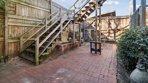 A wooden staircase leading up to a wooden deck with a brick pathway.
