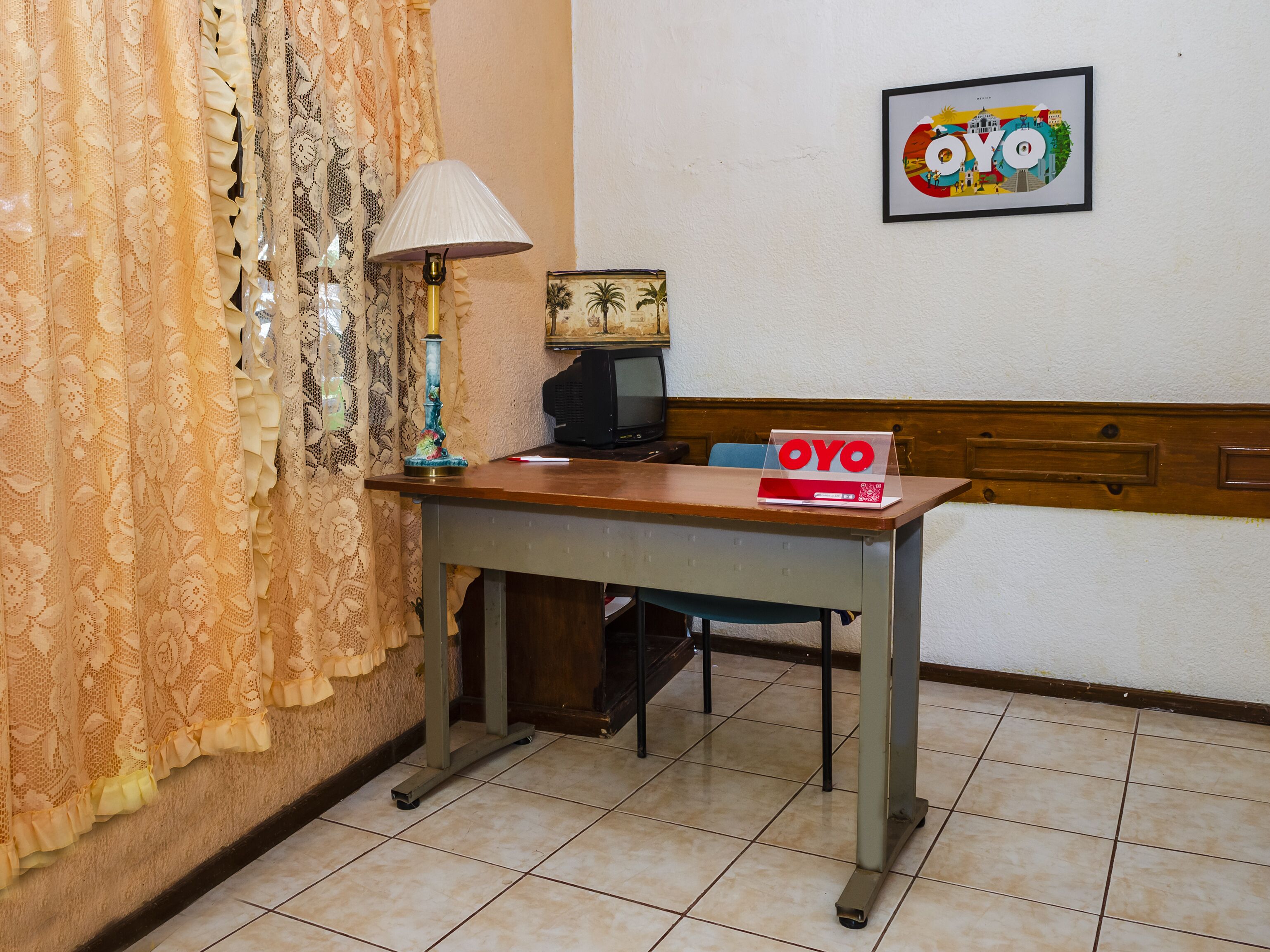 A small room with a wooden table, a lamp, a television, and a framed picture on the wall.