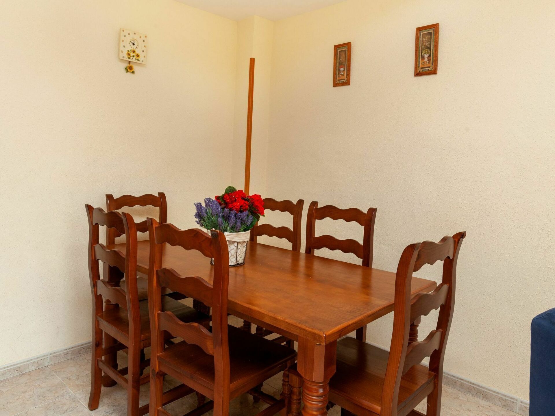 A dining area with a wooden table and six chairs. A vase with flowers is placed on the table.