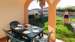 Un comedor con una mesa dispuesta para cuatro personas, rodeada de sillas, y vista a un patio trasero con una parrilla.