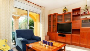 Una sala de estar con un sofá, una mesa de centro con aperitivos, un televisor, armarios de madera y vistas a través de un ventanal.