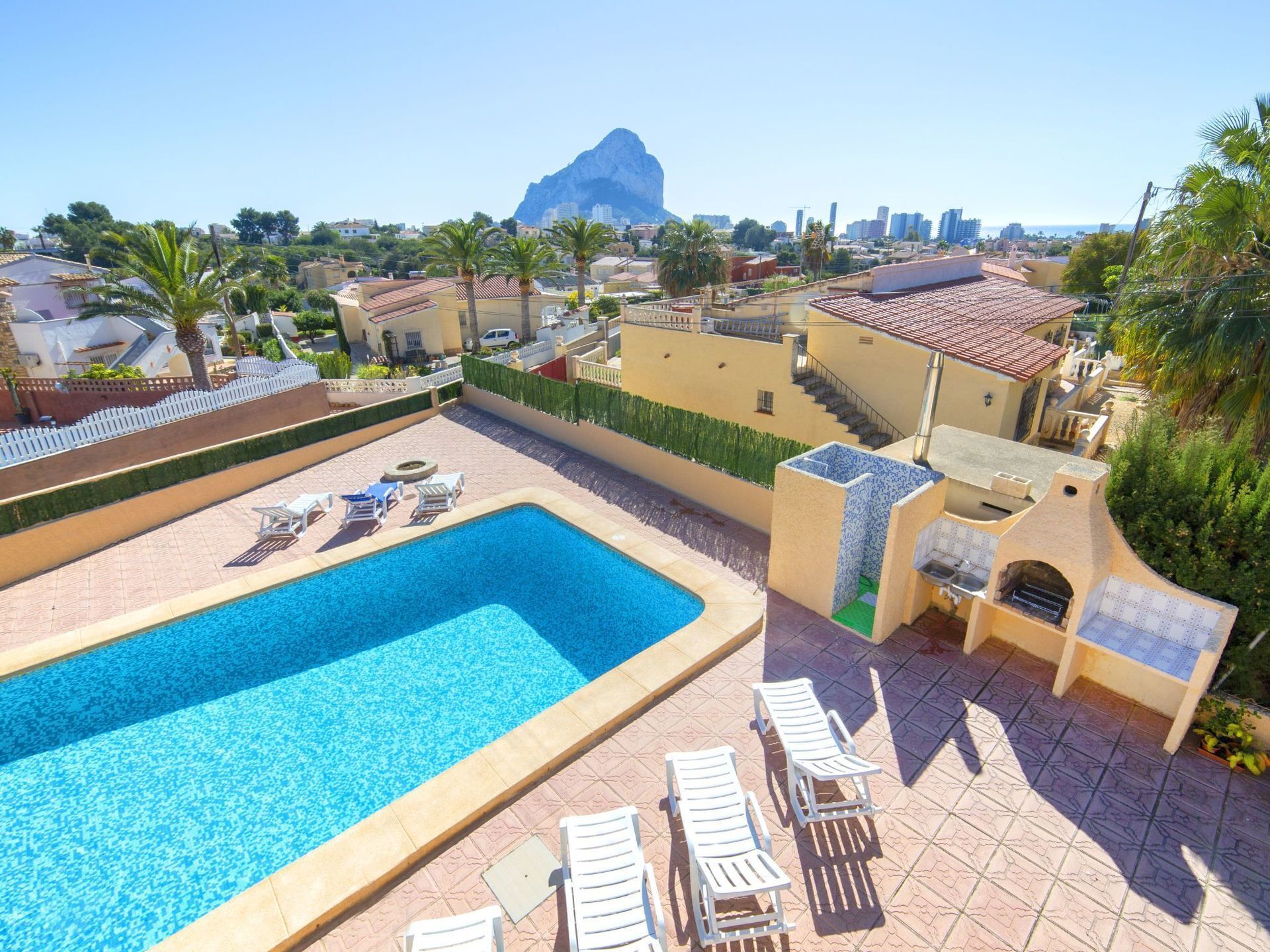 A swimming pool with lounge chairs, a view of a mountain, and a cityscape in the background.