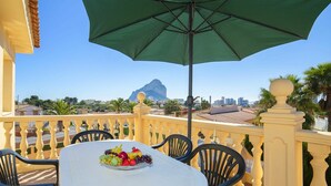 Een balkon met een tafel gedekt voor een maaltijd, inclusief een fruitschaal, onder een groene parasol.