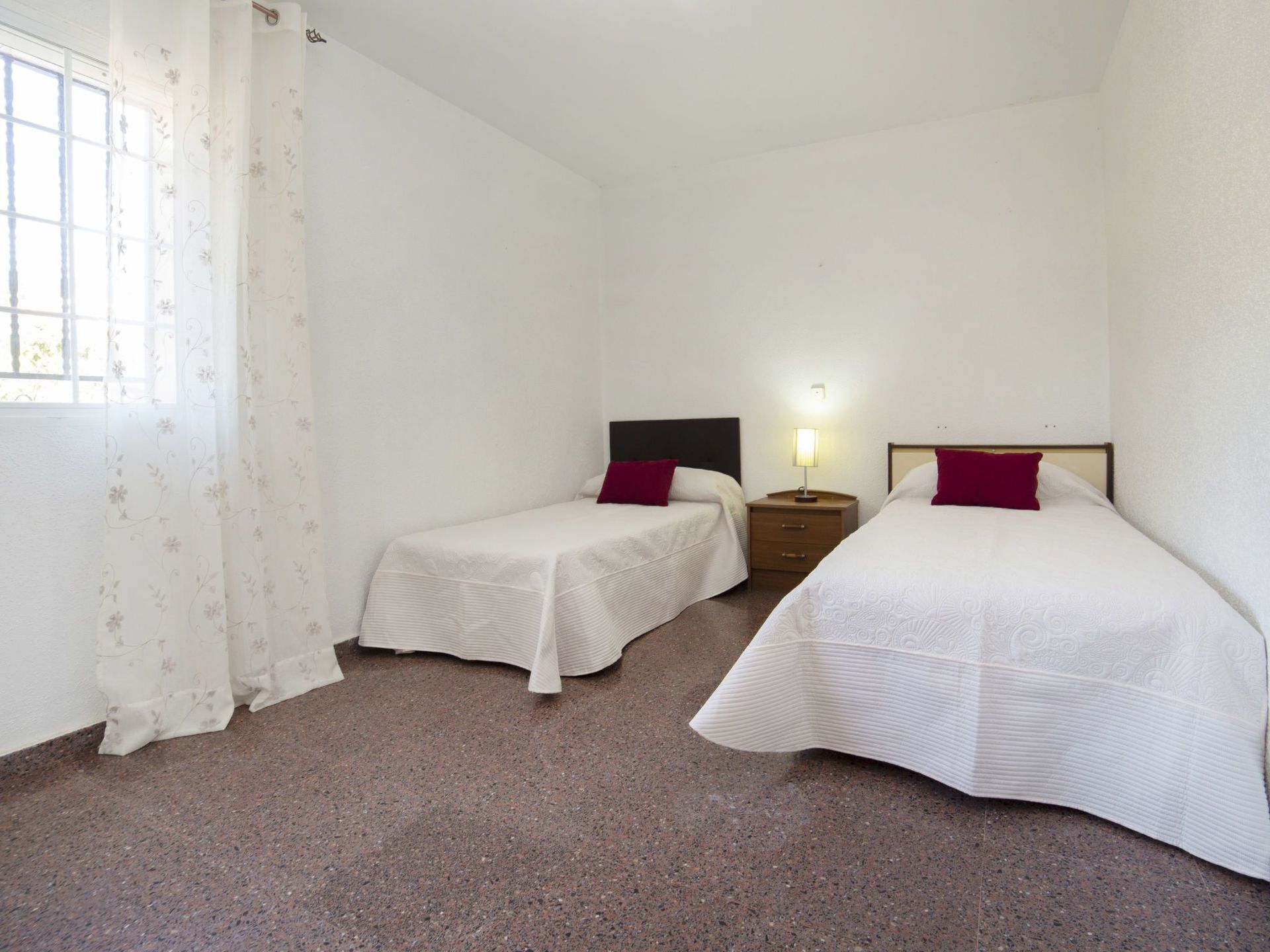 Een kamer met twee eenpersoonsbedden, een nachtkastje met lamp en een raam met gordijnen.