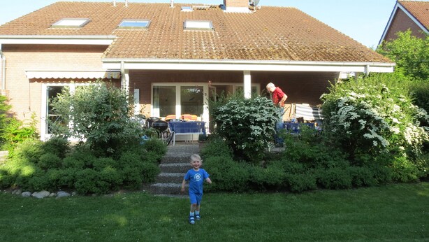 A house with a tiled roof, a covered porch, and a front yard with a child playing.