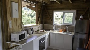 Eine kleine Küche mit weißen Schränken, einer eingebauten Mikrowelle, einem Edelstahlkühlschrank und einem Fenster mit Blick auf Grünflächen.