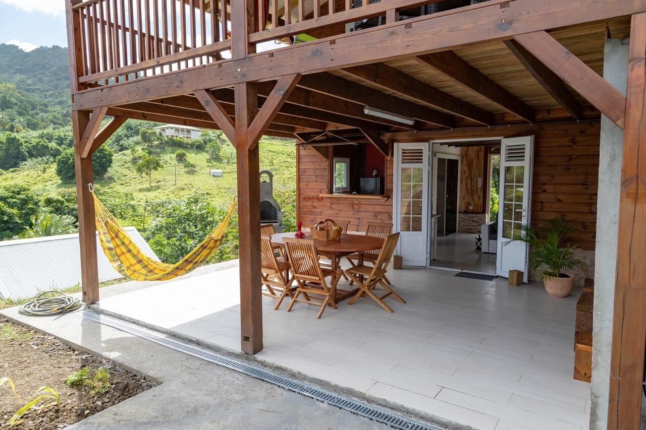 Eine Holzterrasse mit Tisch und Stühlen, einer Hängematte und Blick auf eine üppige, grüne Landschaft.
