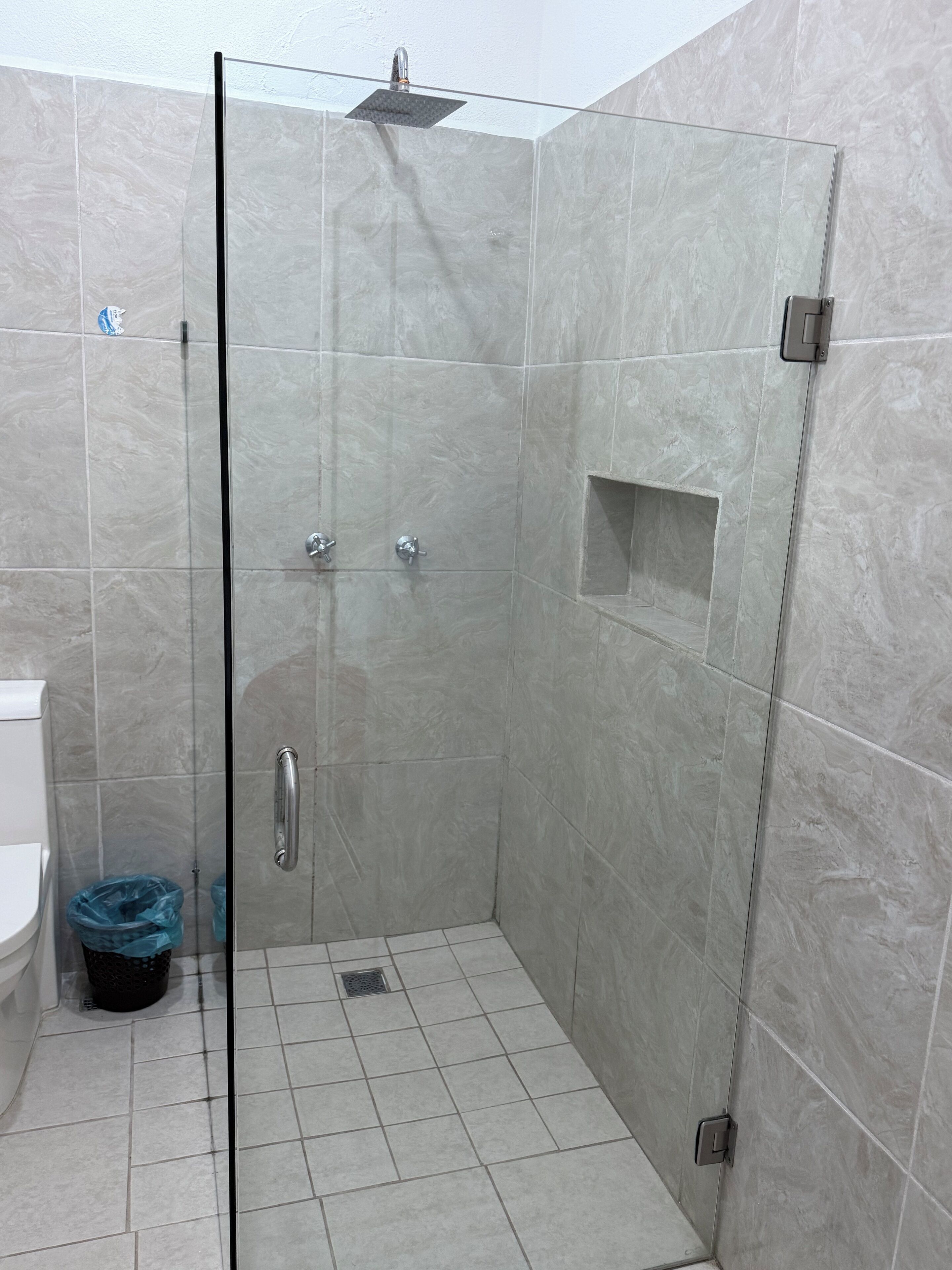 A modern bathroom with a glass-enclosed shower, a toilet, and a trash bin.