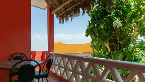 A balcony with a table and chairs, a thatched roof, and a view of the sky and buildings. - Hotel y Bungalows Bugambilias (San Patricio Melaque)