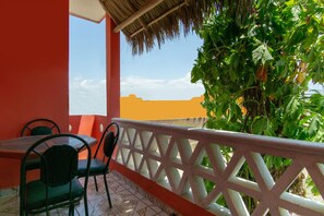 A balcony with a table and chairs, a thatched roof, and a view of the sky and buildings. - Hotel y Bungalows Bugambilias (San Patricio Melaque)