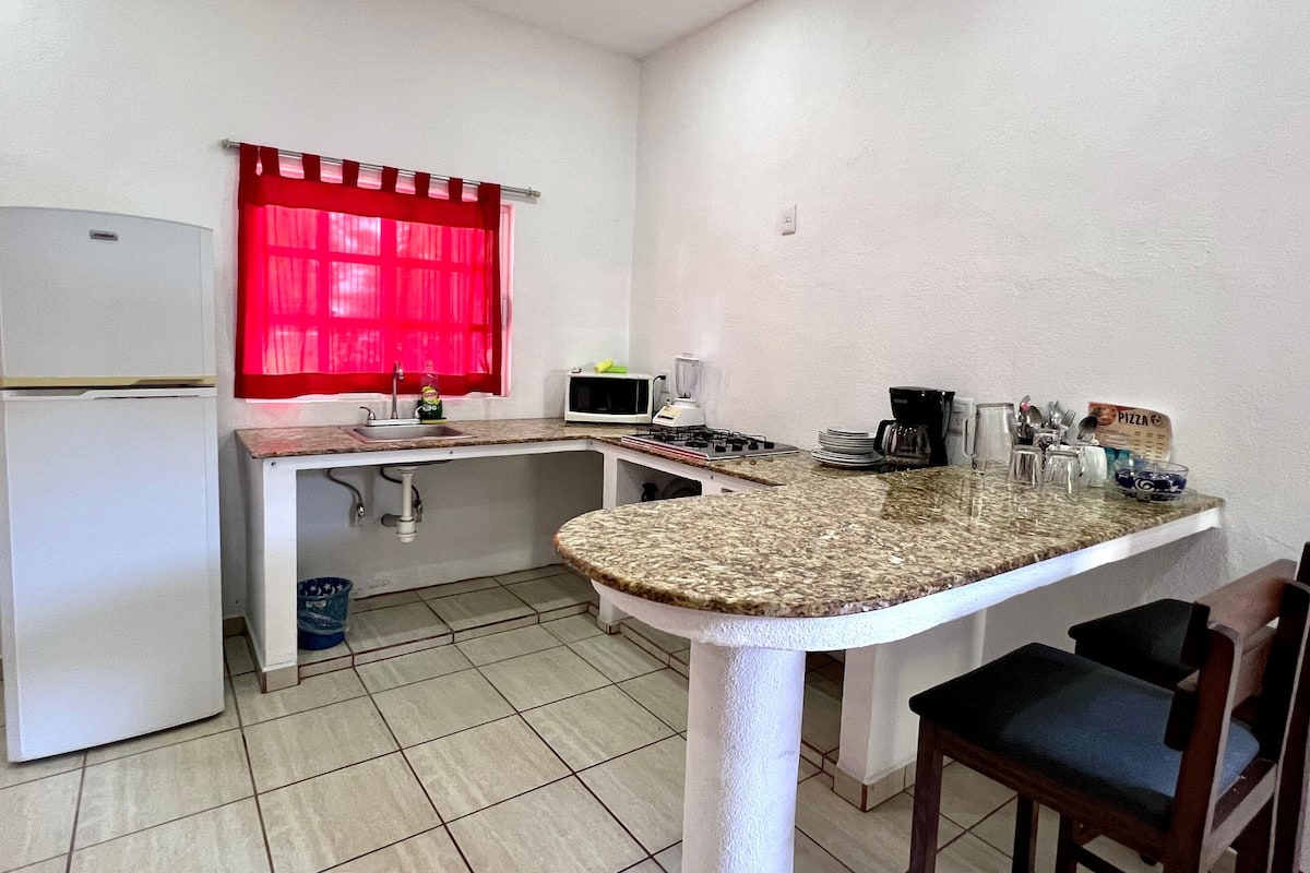 A compact kitchen with a refrigerator, sink, microwave, stove, and a small dining area with chairs.