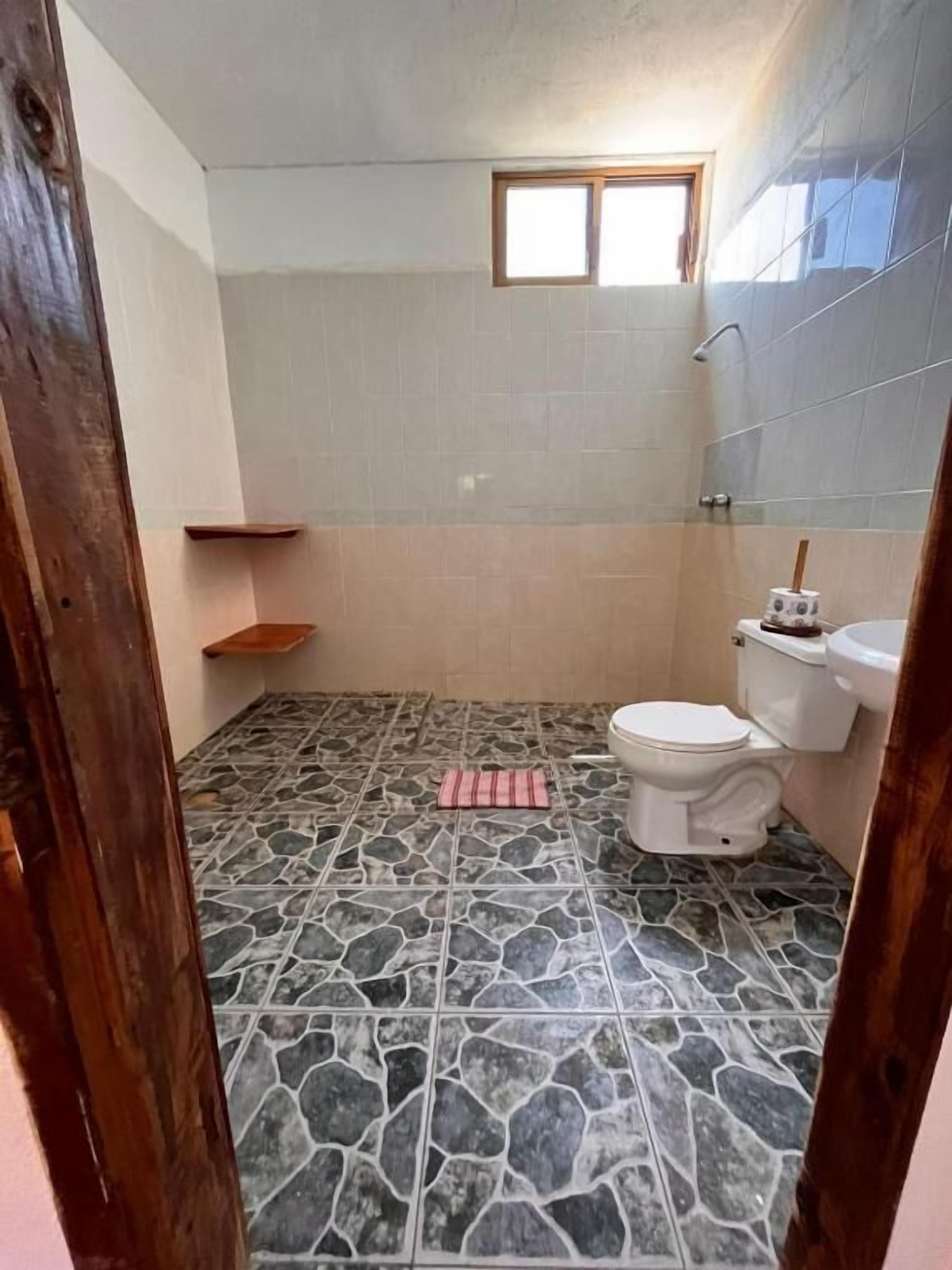 Un baño con piso de piedra, inodoro, lavamanos y un pequeño ventanal.