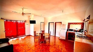 A spacious living area with a red tiled floor, a dining table with chairs, a ceiling fan, and a kitchen area with a stove and microwave. - Hotel y Bungalows Bugambilias (San Patricio Melaque)