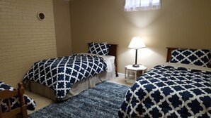 Un dormitorio con dos camas, una mesita de noche con lámpara, una silla y una ventana con cortinas.