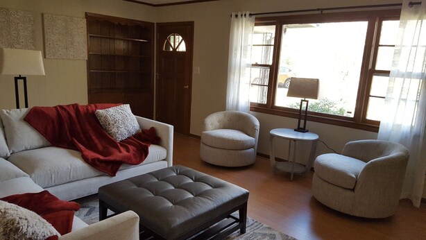 Una sala de estar con sofá, reposapiés, dos sillones, una mesita y una estantería.