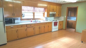 Una cocina con armarios de madera, microondas, estufa y una ventana con cortinas.