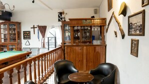 Een biljartkamer met een pooltafel, lederen stoelen, een houten kast en diverse wanddecoraties, waaronder een kruis en ingelijste foto's.