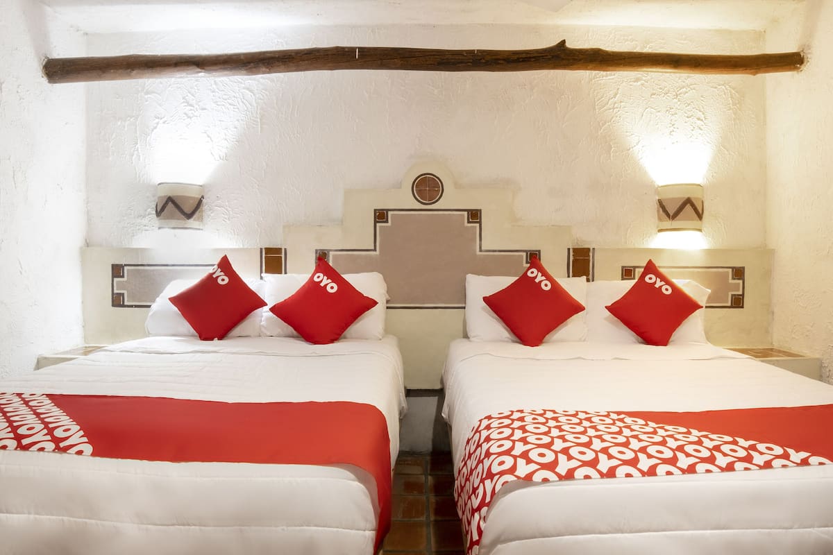 Una habitación de hotel con dos camas, cada una con ropa de cama roja y blanca, y una viga de techo de madera.