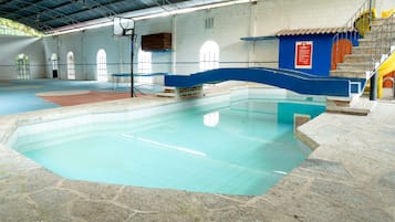 Ein hallenbad mit blauer und roter Liegefläche, Steinboden und einer Treppe, die zu einer gelben Rutsche führt.